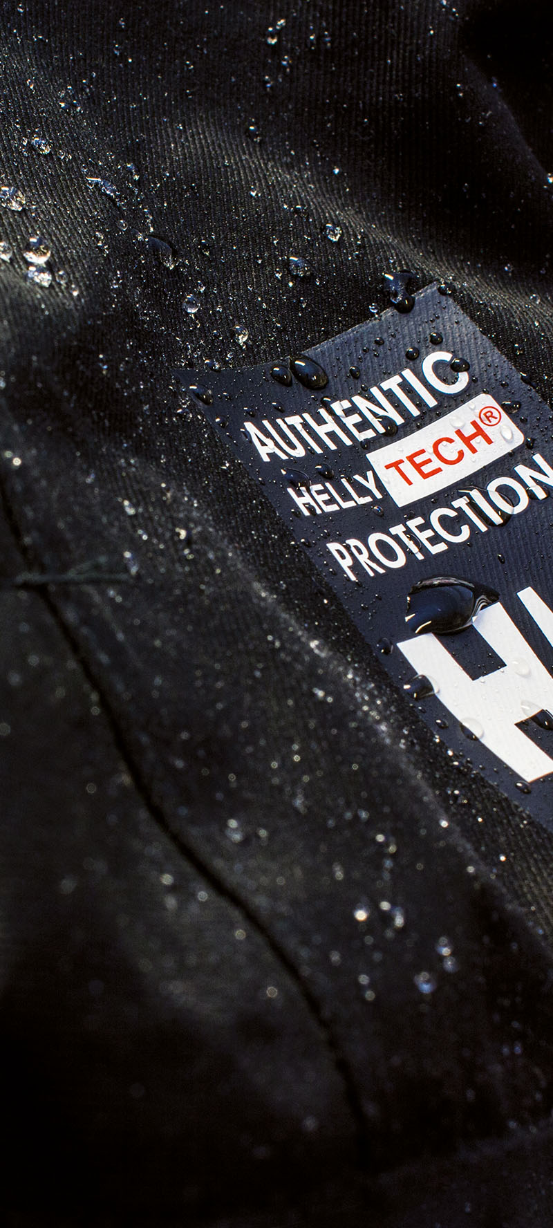 Ausschnitt eines schwarzen Jackenärmels mit abperllenden Regentropfen der Marke Helly Hansen mit der Aufschrift "Authentic Helly Tech Protection"