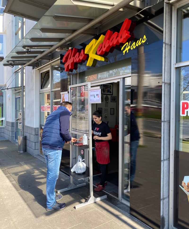 Mann kauft einen Kebab. Zwischen Verkäuferin und Käufer steht eine Schutzwand