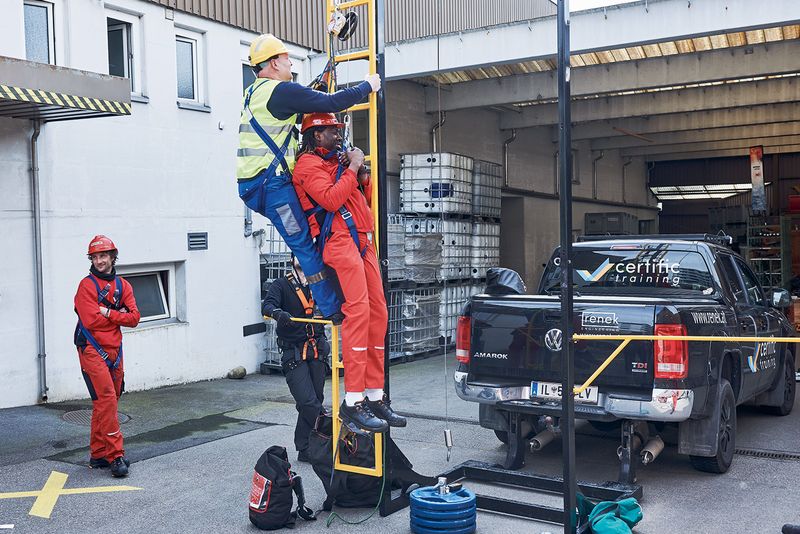 Drei Arbeiter in Schutzbekleidung im Einsatz auf Leiter während Certific-Sicherheitstraining; Truck im Hintergrund