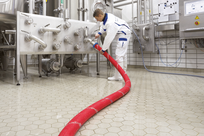Arbeiter in weißer Schutzbekleidung verbindet roten Getränkeschlauch mit Füllanlage