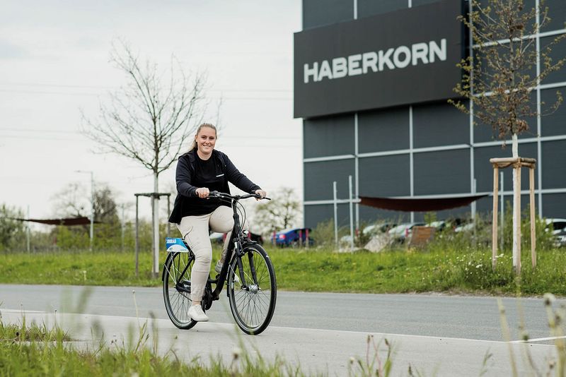 Haberkorn Mitarbeiterin vor Haberkorn Firmengebäude auf dem Weg zur Arbeit mit dem Fahrrad